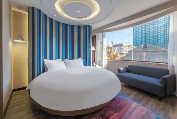 Une chambre d’hôtel moderne avec un grand lit, un canapé, une vue sur la ville et un mur à rayures.