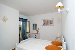 A bedroom with a bed, two bedside tables, a dresser, a mirror, and two wall-mounted lamps.