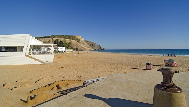 A beach with a white building, steps leading to it, and a sandy area with a few people. - Casa Alma Mar, 2 minutes' walk to the beach (Luz)