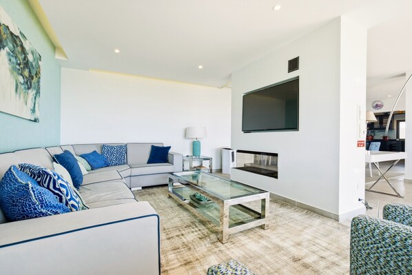 A modern living room with a sectional sofa, a glass coffee table, and a flat-screen TV mounted on the wall.
