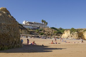Een strand met een gebouw op de achtergrond, zandstrand en palmbomen.