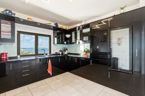 A modern kitchen with black cabinetry, a coffee machine, and a view of the sea.