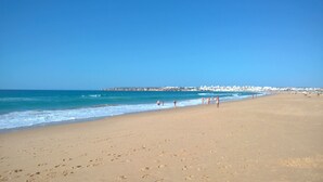 A wide sandy beach with footprints, a clear blue sky, and a distant shoreline with buildings. - Quinta Marina with sea views, private pool and garden (Lagos)