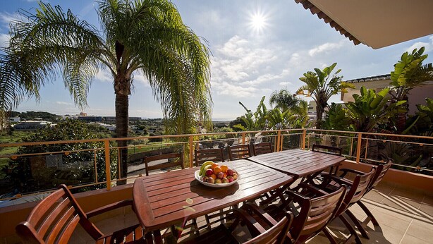 A wooden table with chairs on a balcony, a bowl of fruit, and a view of the cityscape. - Quinta Marina with sea views, private pool and garden (Lagos)