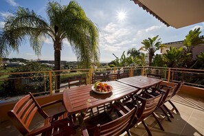 A wooden table with chairs on a balcony, a bowl of fruit, and a view of the cityscape. - Quinta Marina with sea views, private pool and garden (Lagos)
