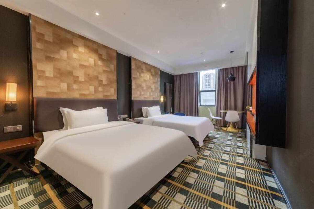 Une chambre d’hôtel avec deux lits, un mur en bois à texture, une moquette à motifs et une fenêtre avec des rideaux.