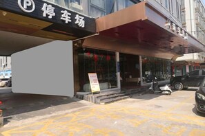 A parking lot with a building entrance, a signboard, and a scooter parked outside. - Huanyu Hotel (Lingshan Bus Terminal) (Lingshan)