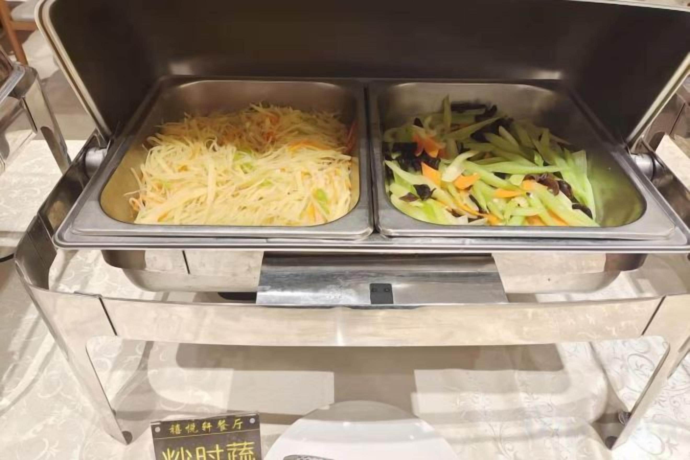 Buffetpöydässä on kaksi tarjoilualustaa: toisessa on suikaloituja kasviksia ja toisessa salaattia.