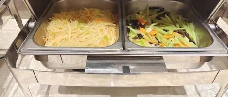 Buffetpöydässä on kaksi tarjoilualustaa: toisessa on suikaloituja kasviksia ja toisessa salaattia.