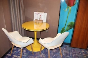 A room with a yellow round table and two white chairs, a menu stand, and a wall with a rose painting. - Huanyu Hotel (Lingshan Bus Terminal) (Lingshan)