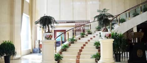 A grand staircase with multiple landings, flanked by potted plants and columns, leading to an upper floor.