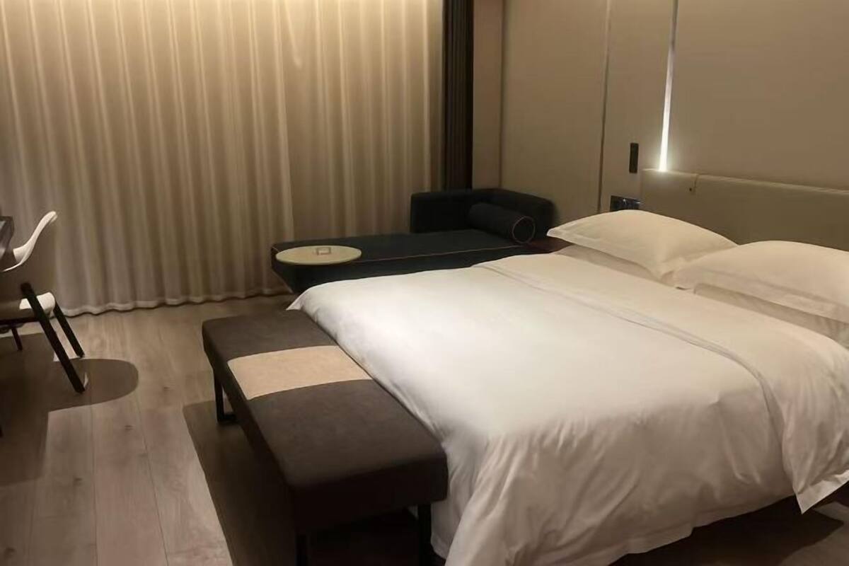 Hotellihuone, jossa on sänky, penkki, tuoli ja pieni pöytä.