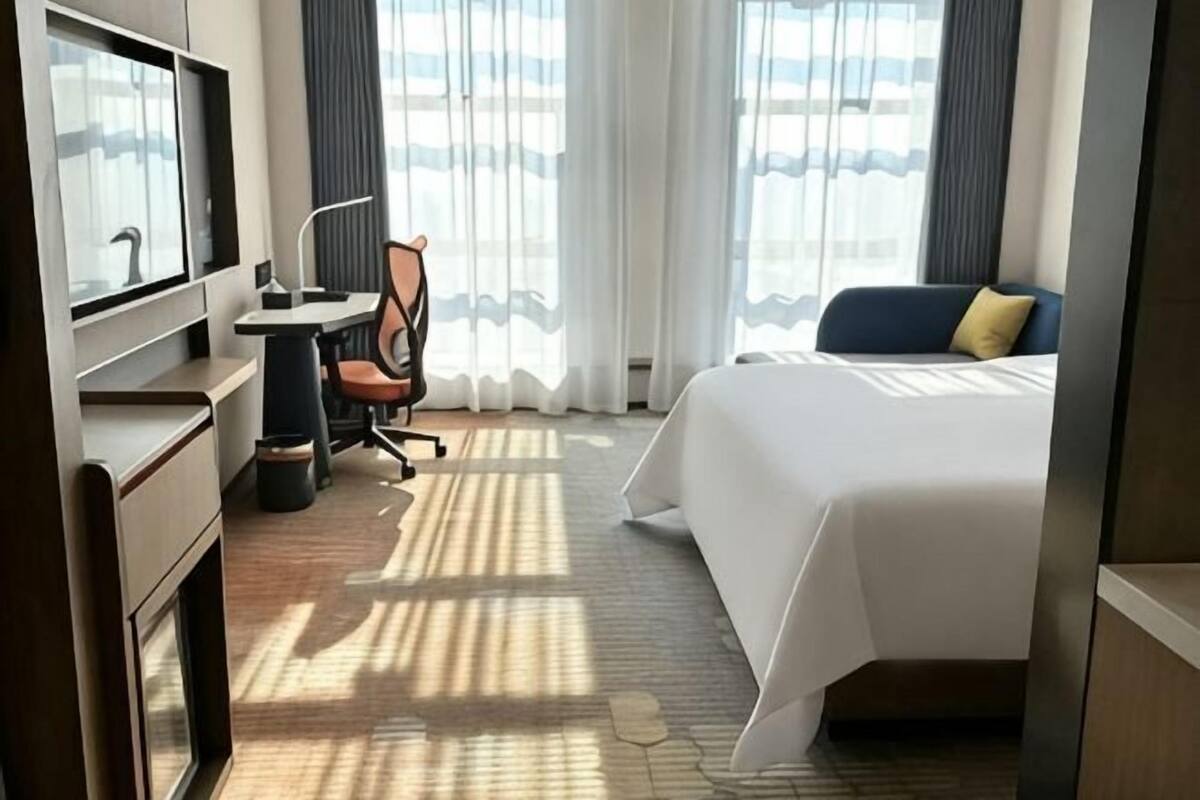 Hotellihuone, jossa on sänky, työpöytä, tuoli ja suuri ikkuna, jossa on verhot.