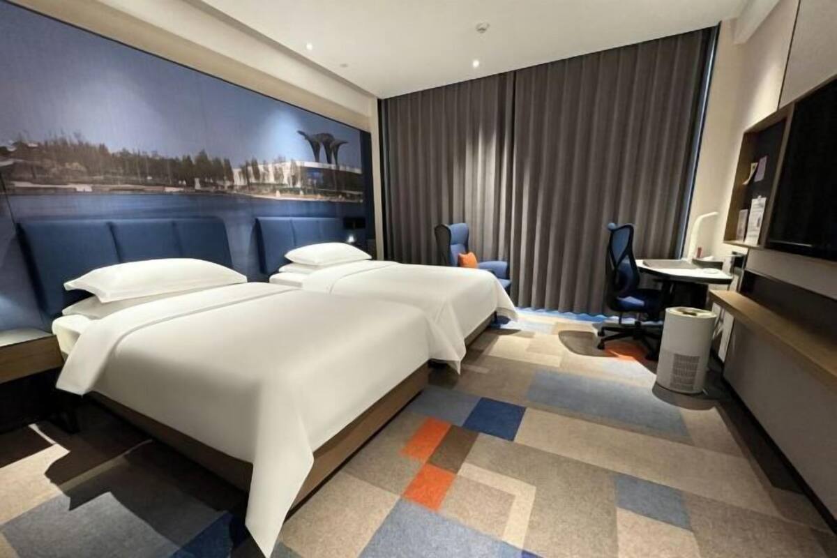 Hotellihuone, jossa on suuri sänky, työpöytä, tuoli, televisio ja ikkunasta avautuva näkymä kaupungin ylle.