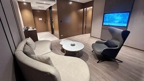A modern hotel room with a sofa, armchair, small round table, and a television screen. - Jindu Hotel (Gucheng)