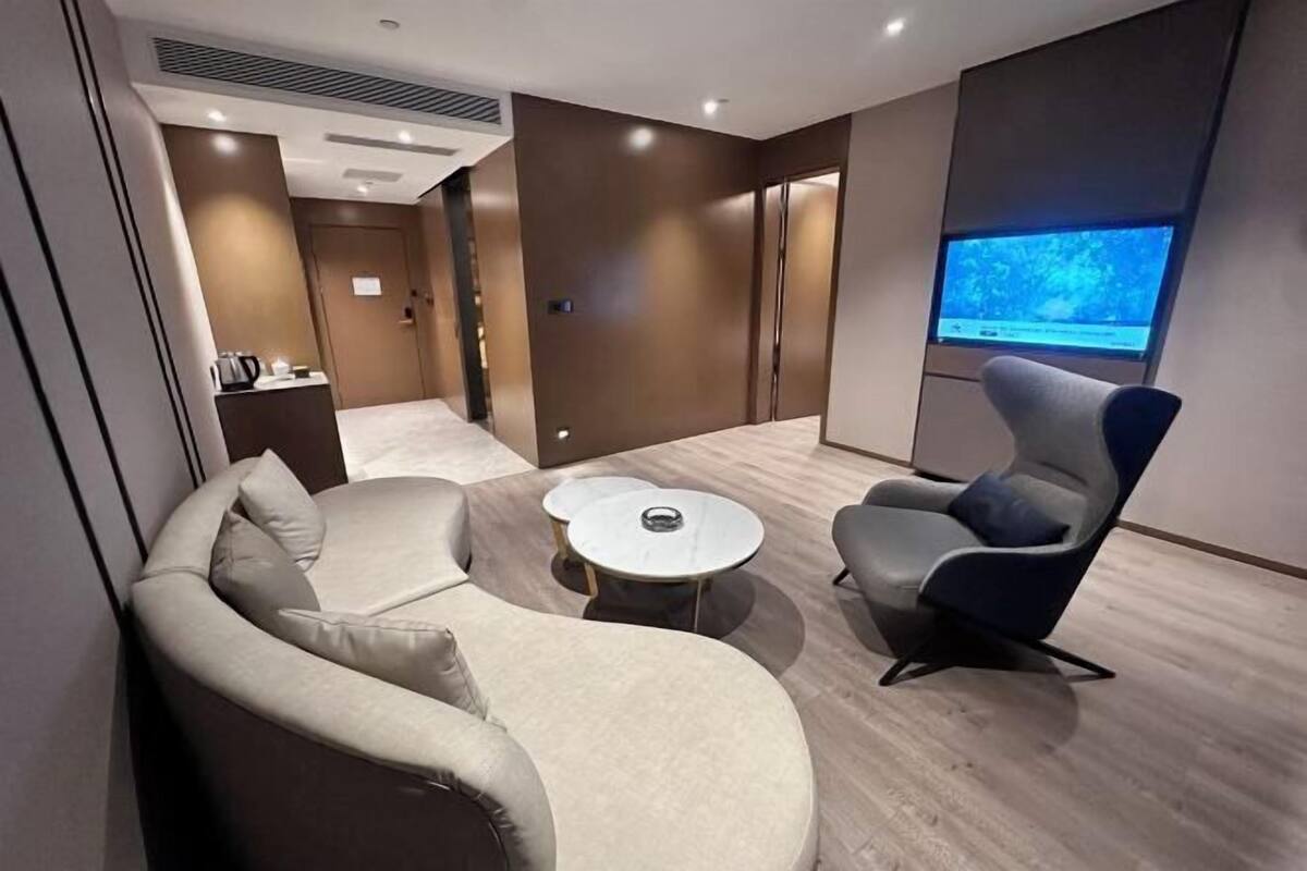 Moderni hotellihuone, jossa on sohva, nojatuoli, pieni pyöreä pöytä ja televisio.