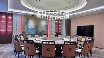 A conference room with a round table, chairs, a chandelier, a painting, and a TV on the wall.