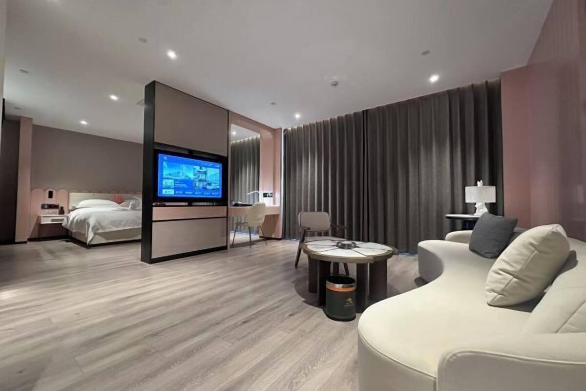 Moderni hotellihuone, jossa on sänky, televisio, sohva, pieni pöytä ja työpöytä tuolilla.