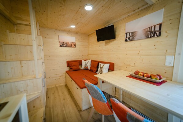 A cozy wooden cabin with a sofa, a dining table with apples, and a TV mounted on the wall.