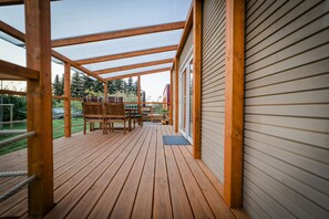 A wooden deck with a covered patio area, wooden furniture, and a view of the outdoors.