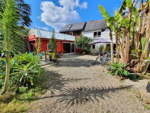 A house with a gravel driveway, a red and white exterior, and a garden with various plants and a bicycle. - Maison typique pour 6 personnes, jardin clos et fleuri, proche plage (Treffiagat)