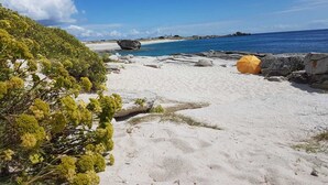 Een strand met wit zand, een grote rotsformatie en een helderblauwe lucht.
