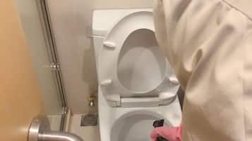 Un inodoro con la tapa cerrada, una tubería visible y un objeto pequeño en la pared.