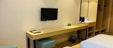 A hotel room with a bed, a desk with a chair, a television, and a wardrobe.