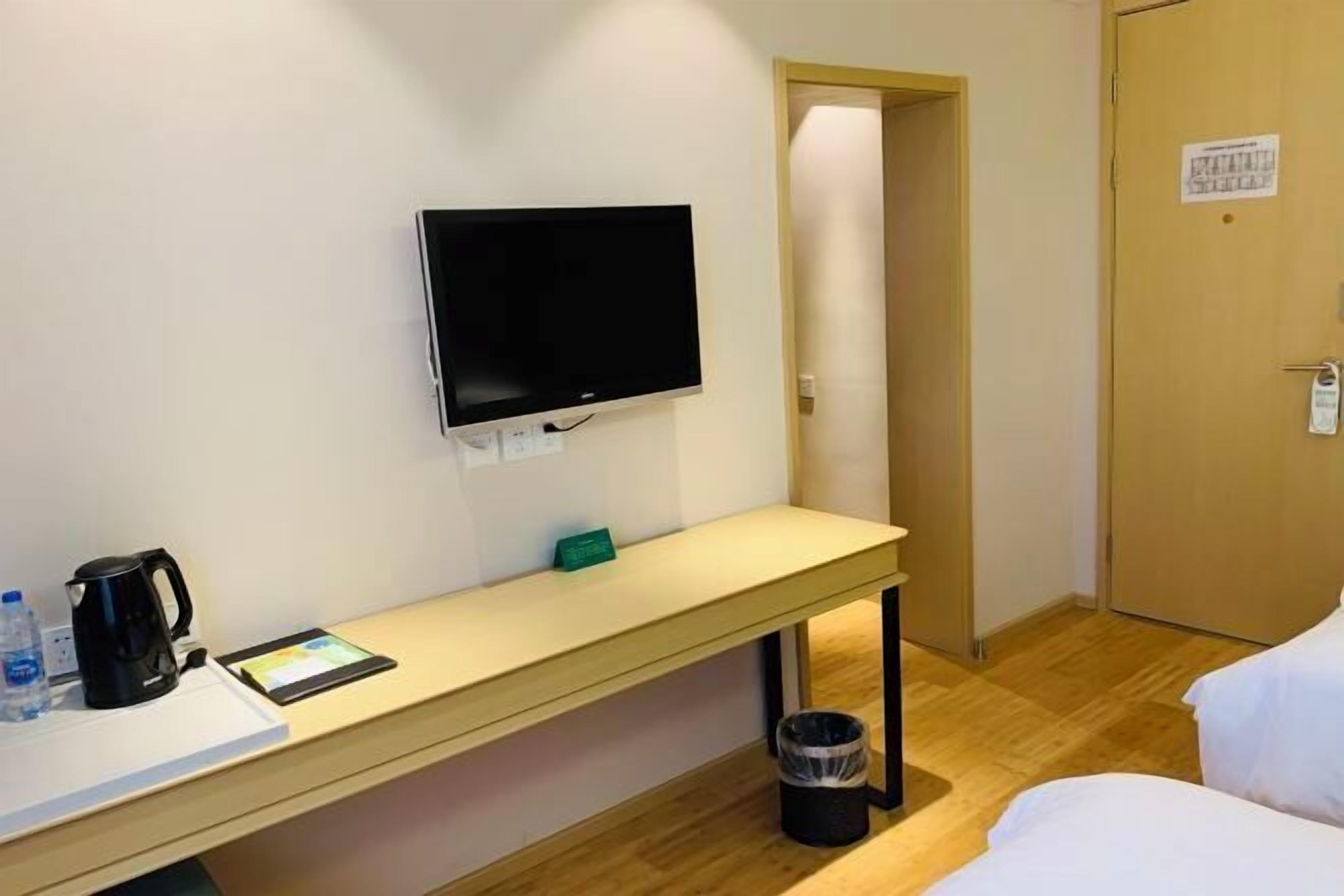 Hotellihuone, jossa on sänky, työpöytä, kahvinkeitin, tabletti, seinälle asennettu televisio ja roskakori.