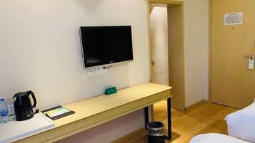 Hotellihuone, jossa on sänky, työpöytä, kahvinkeitin, tabletti, seinälle asennettu televisio ja roskakori.