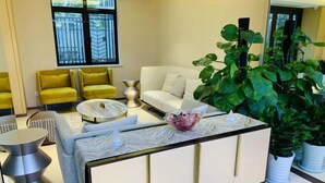 Un salon moderne avec un canapé, des fauteuils jaunes, une table basse et une grande plante.
