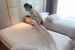 A person adjusting a bedspread in a hotel room with a headboard and a window with curtains. - Shanghai Sanhang Hotel (Shanghai)