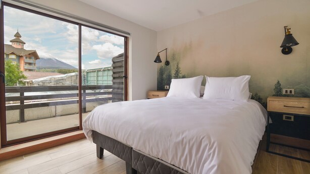 A bedroom with a large bed, a nightstand, a lamp, and a view of a mountain through a sliding door. - Mawün Hotel Pucón (Pucón)
