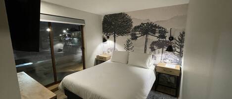 A bedroom with a bed, bedside tables, a desk, and a large window.