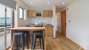 A modern kitchen with wooden cabinets, a microwave, and a wooden dining table with stools. - Mawün Hotel Pucón (Pucón)