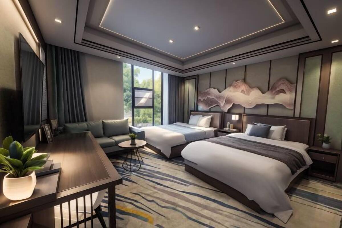 A modern hotel room with a large bed, a sofa, a desk, and a large window.