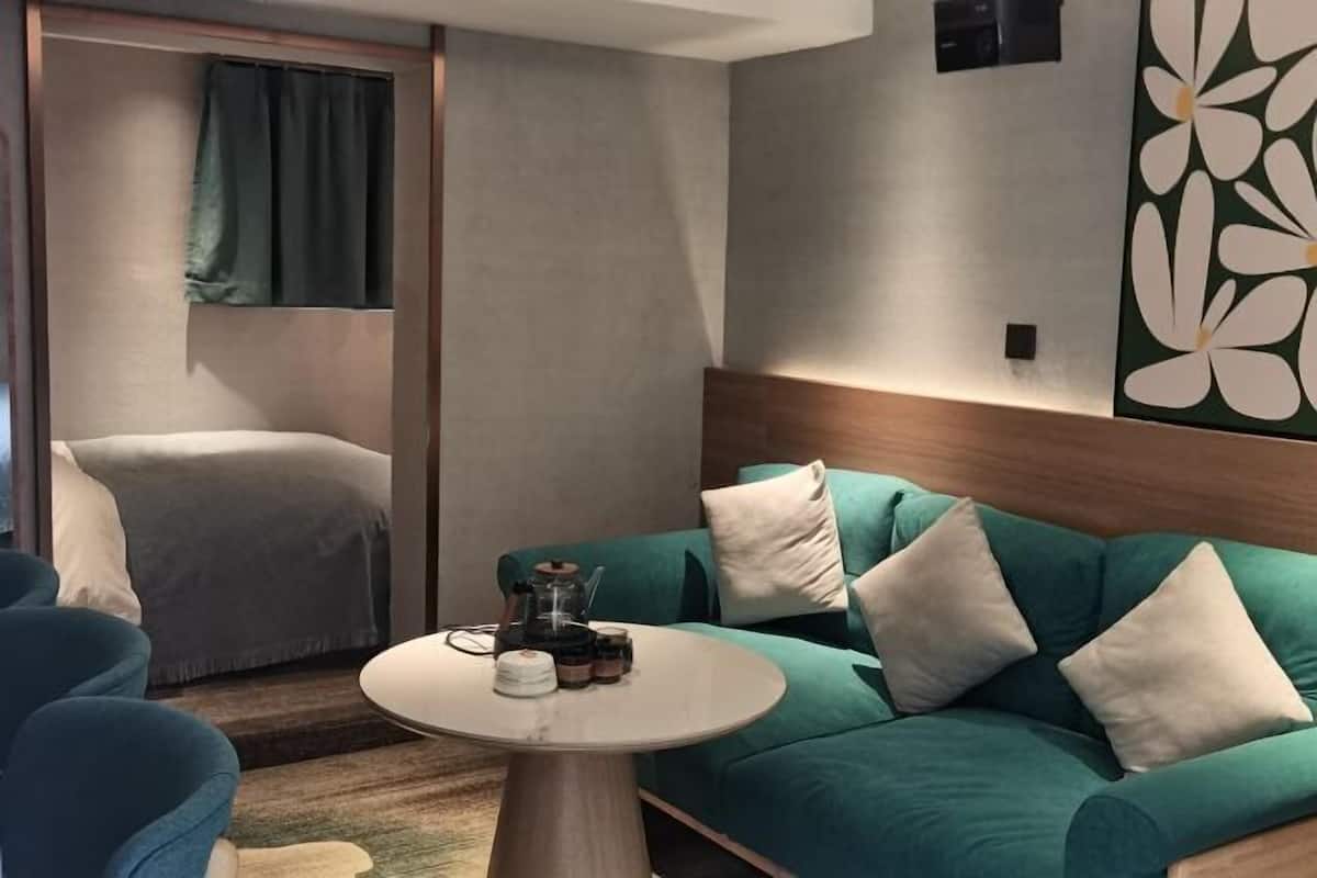 A modern hotel room with a teal sofa, a round coffee table, and a large abstract floral wall art piece.