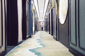 Un pasillo de hotel con piso alfombrado, puertas a ambos lados y una persona alejándose de la cámara.