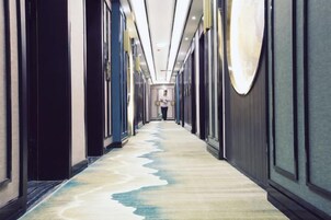 Un pasillo de hotel con piso alfombrado, puertas a ambos lados y una persona alejándose de la cámara.