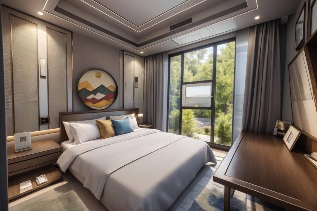 A modern hotel room with a large bed, a desk, and a view of greenery through the window.