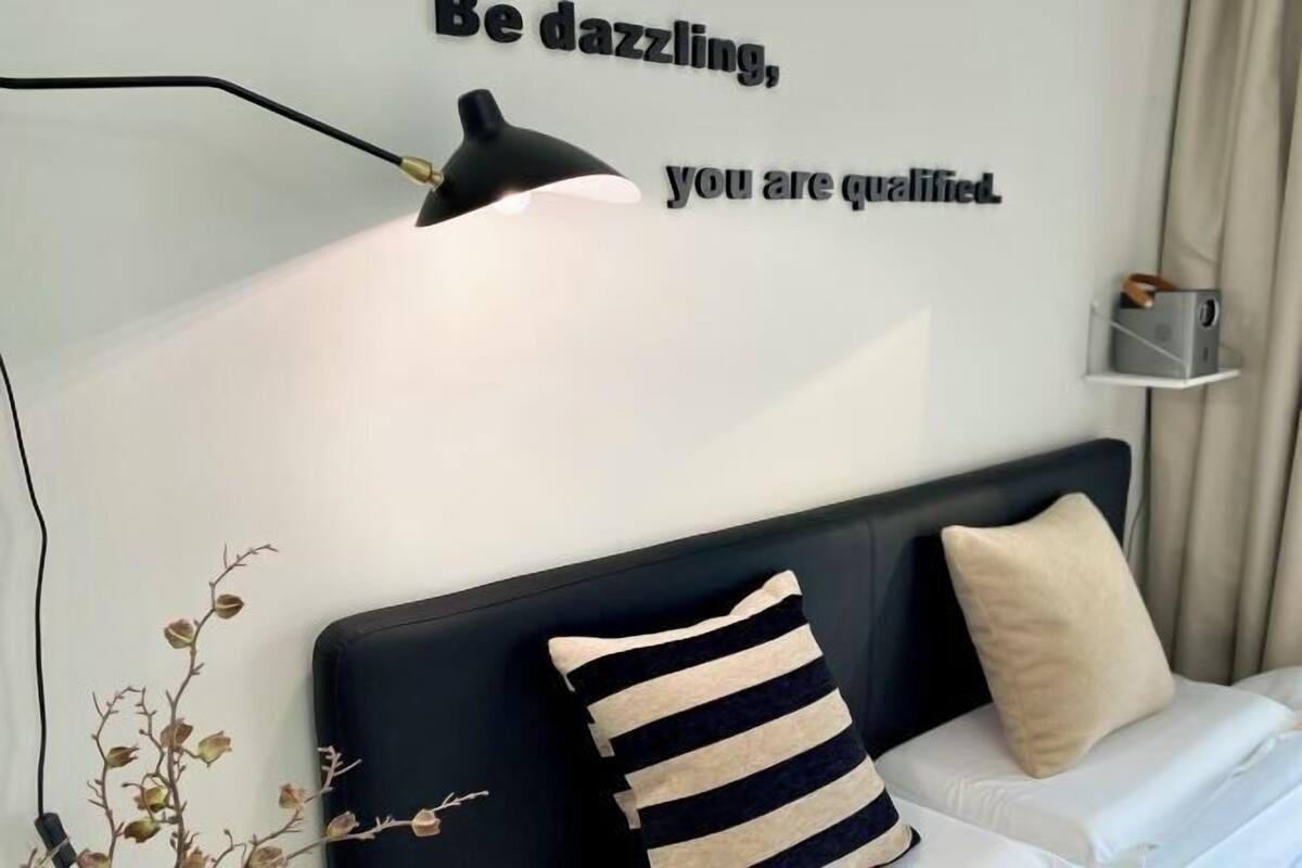 A modern bedroom with a black headboard, a bedside lamp, and a motivational quote on the wall.