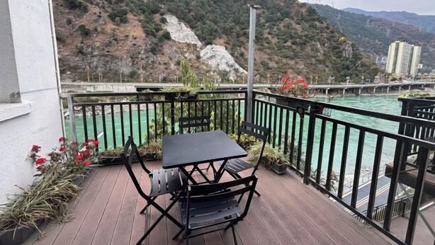 Ein Balkon mit Tisch und Stühlen mit Blick auf einen Fluss und Berge.