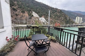Un balcón con mesa y sillas, con vista a un río y montañas.