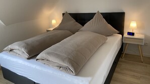 A neatly made bed with two pillows and a digital clock on a bedside table. - Modern holiday apartment for 2-4 people, free WLAN, summer/winter offers (Norden)