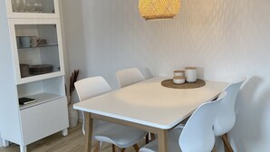 A dining area with a white table, light blue chairs, a woven pendant light, and a white cabinet with shelves. - Modern holiday apartment for 2-4 people, free WLAN, summer/winter offers (Norden)