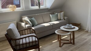 A modern loft bedroom with a sloped ceiling, a large window, a sofa, a chair, and a small round table. - Modern holiday apartment for 2-4 people, free WLAN, summer/winter offers (Norden)