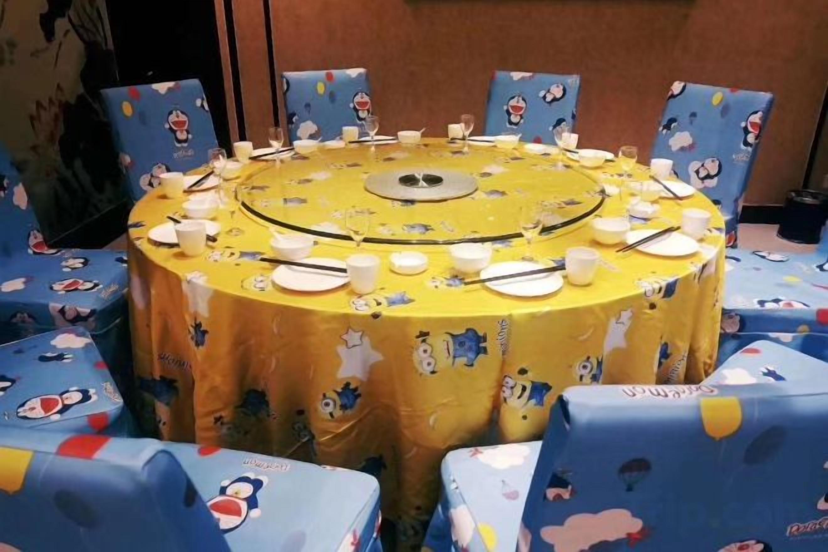 Une table ronde recouverte d’une nappe jaune, entourée de chaises bleues ornées de personnages de dessins animés.