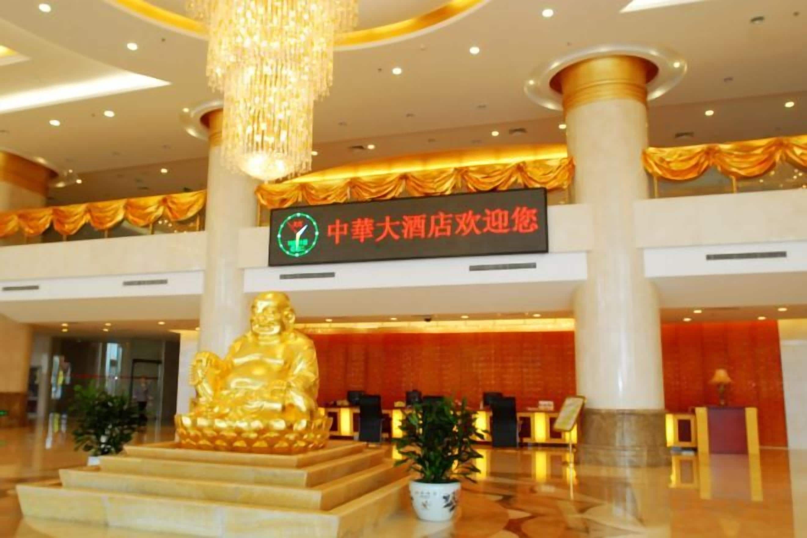 A hotel lobby with a large golden Buddha statue, a reception desk, and a sign indicating a hotel promotion.