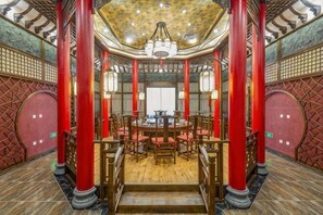 Um interior tradicional com uma mesa redonda central, pilares vermelhos e teto estampado.