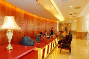 A reception area with a red counter, a lamp, and several chairs. - Mei Di Ya Zhong Hua Hotel (Zhuolu)